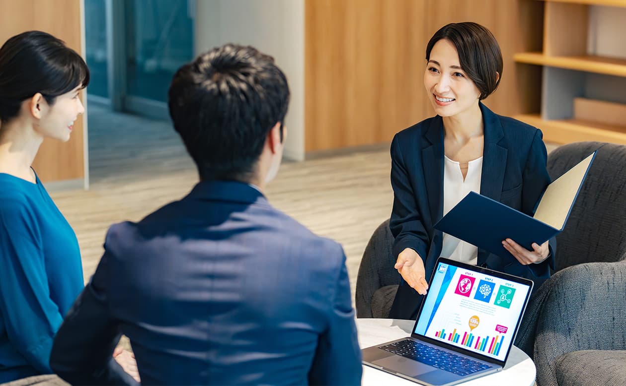 女性と男性がパソコンの前でビジネス会話をしているシーン、オフィス内での打ち合わせ